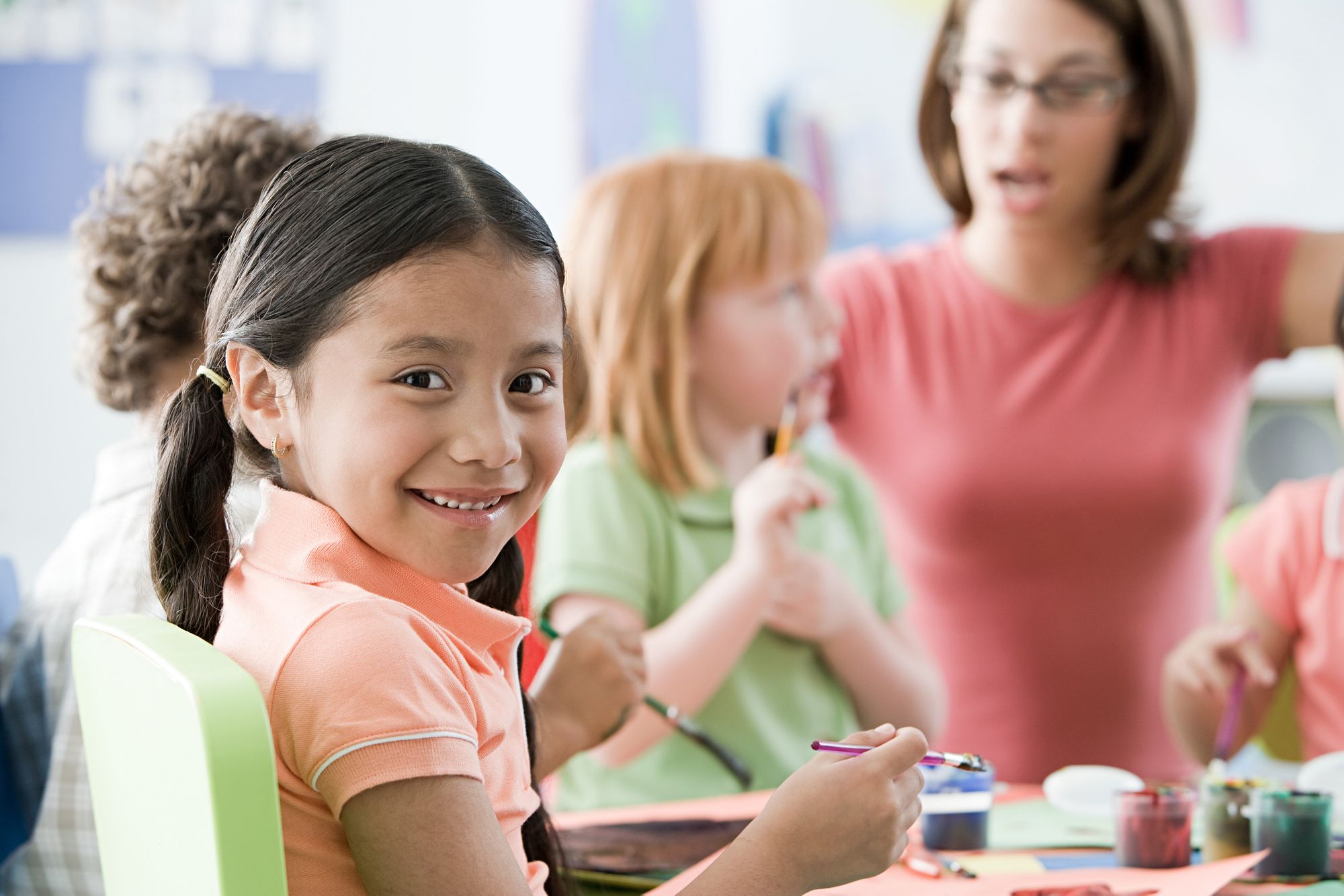 child_girl_at_desk_orange_shirt_teacher_bg.jpg